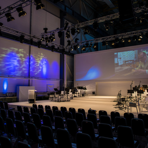 Daimler 75 Jahre PKW: Ansicht einer Orchesterbühne mit leeren Stuhlreihen davor.