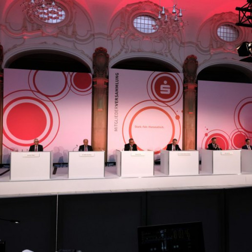 Die Sparkasse Bremen Mitgliederversammlung: Zentraler Blick auf die Bühne, auf der sieben Personen hinter ihren Tischen sitzen.