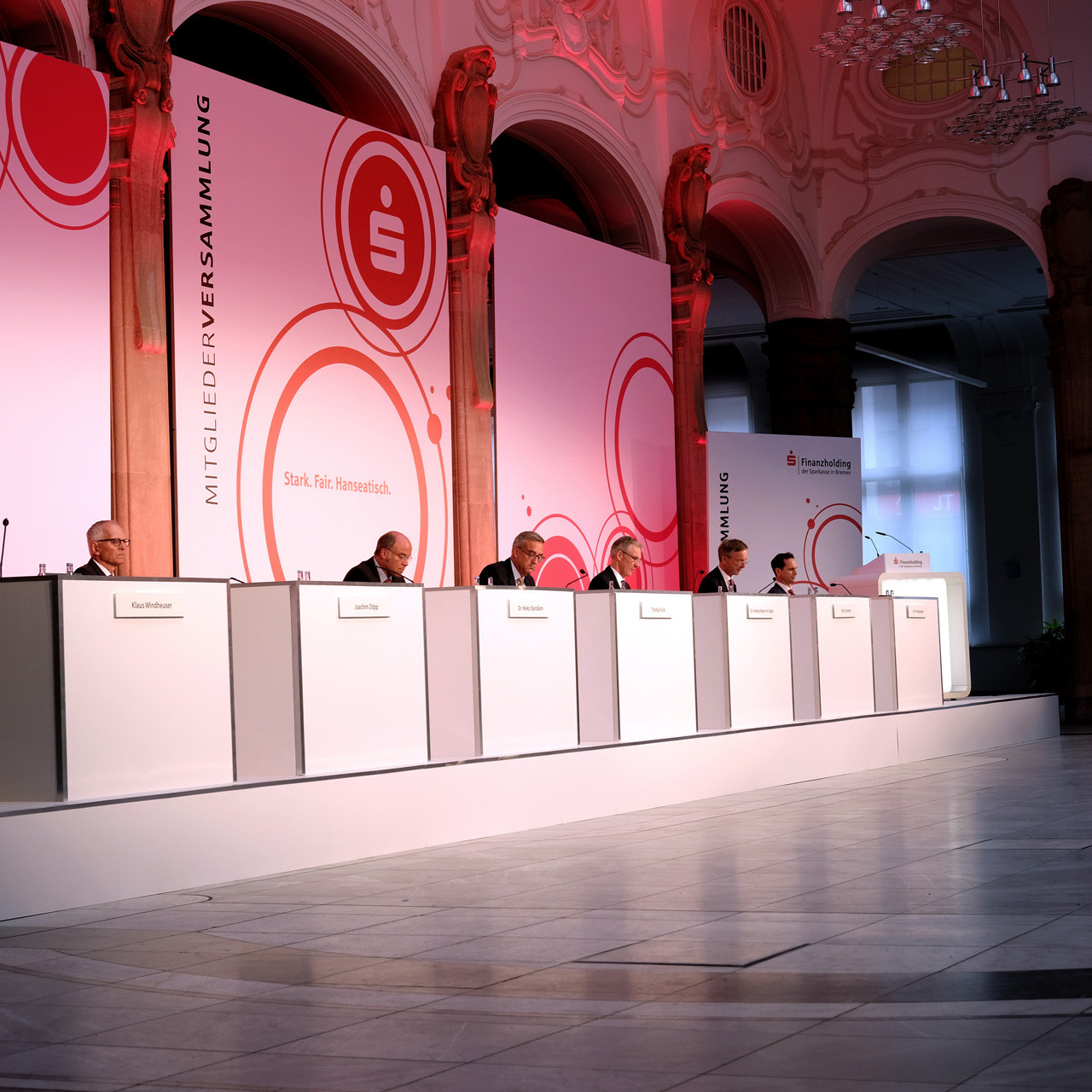 Die Sparkasse Bremen Mitgliederversammlung: Blick auf das Podium auf dem sieben Personen sitzen, jeder Corona Konform mit 1.5 Meter Abstand.