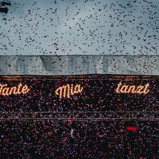 Tante Mia Tanzt: Konfettiregen vor beleuchtetem Festivallogo bei Dämmerung