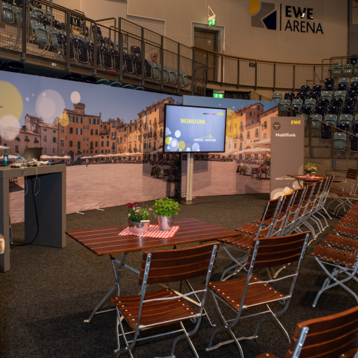 EWE Tel Partnerforum: Blick in einen Workshopbereich. Hier stehen Biergartentische mit Biergartenstühlen im halbkreis um einen Bildschirm.
