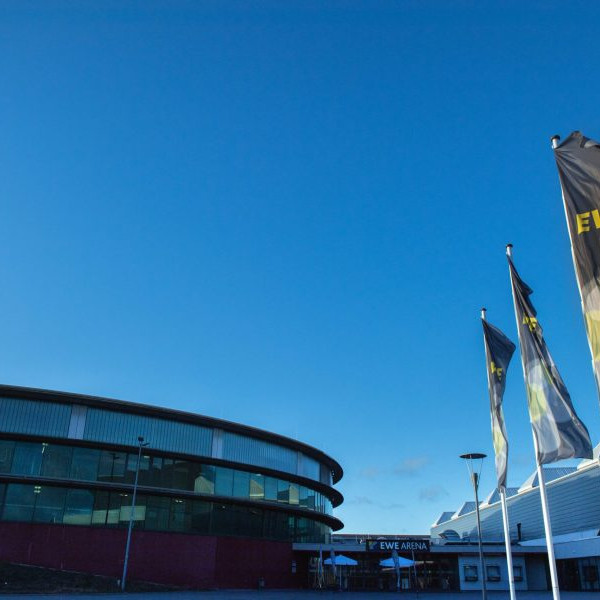 EWE Tel Partnerforum: Aussenansicht der EWE Arena in Oldenburg. Rechts im Bild sin vier Fahnenmasten mit EWE Fahnen.