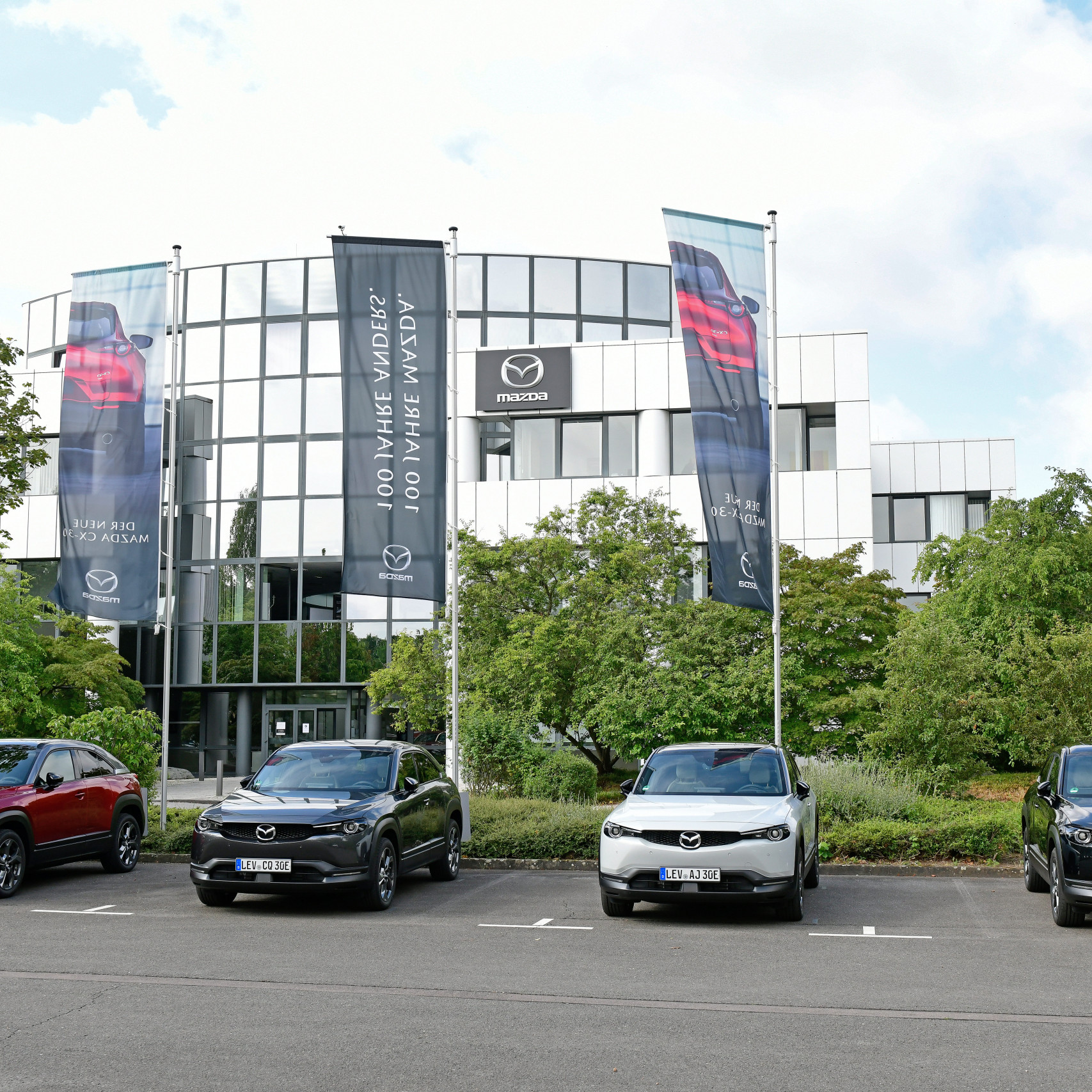 Mazda MX30 Presse Launch: Vier neue Mazda MX30 stehen vor dem Firmengebäude von Mazda.