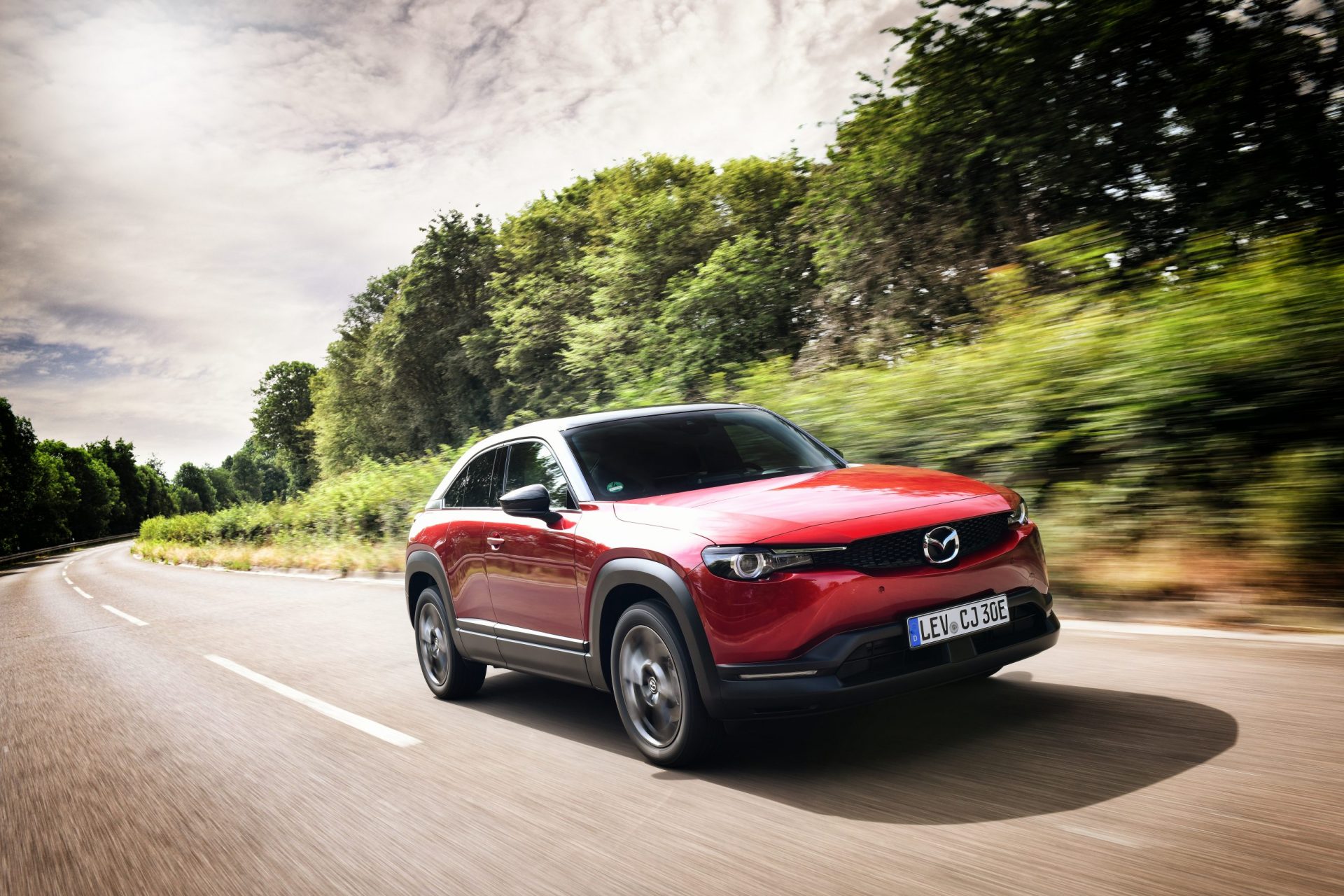 Mazda MX30 Presse Launch: Ein roter Mazda MX30 fährt schnell auf der Strasse durch die Landschaft.