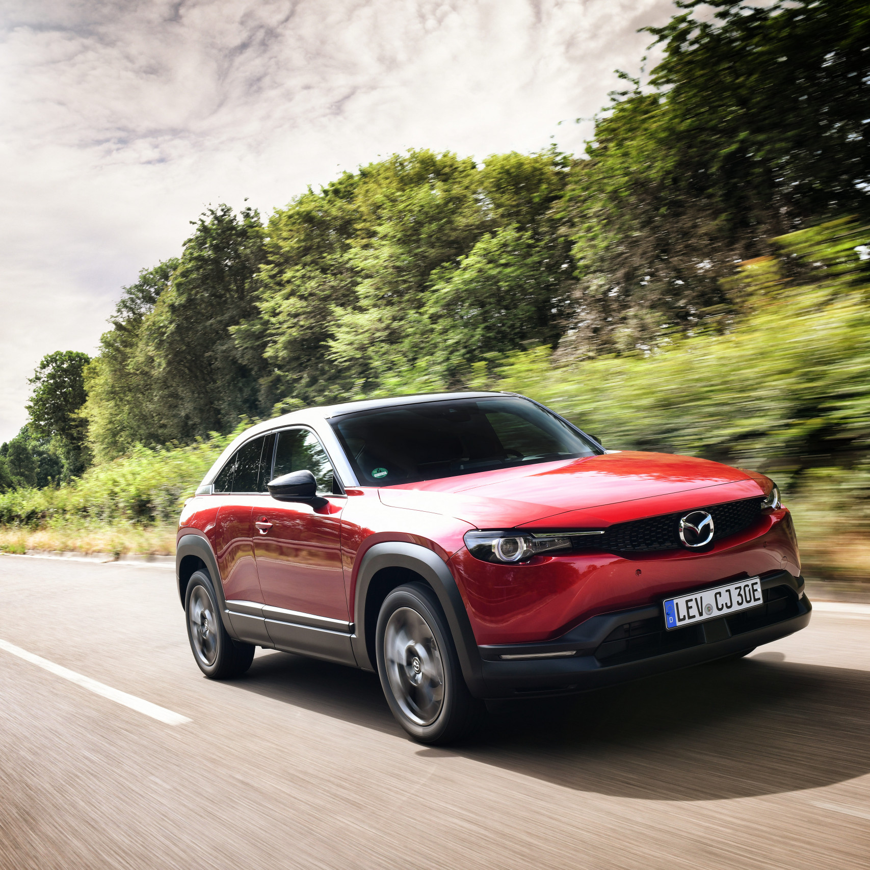 Mazda MX30 Presse Launch: Ein roter Mazda MX30 fährt schnell auf der Strasse durch die Landschaft.