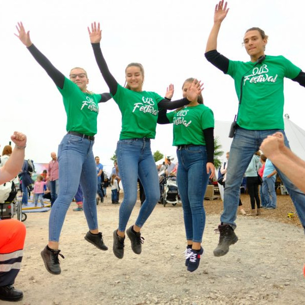 OLB 150 Jahre Festival: Drei junge Frauen und ein junger Mann ,alle im grünen OLB T Shirt, springen in die Luft und heben die Arme dabei.